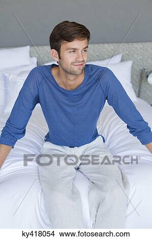 Picture - Man sitting on the bed and smiling. Fotosearch