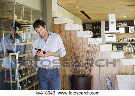 Smiling man looking at a wine bottle View Large Photo Image Stock Image - Smiling man looking at a wine bottle. Fotosearch