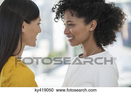 Close-up of two female friends smiling at each other View Large Photo Image Stock Image - Close-up of two female friends smiling at each other. Fotosearch