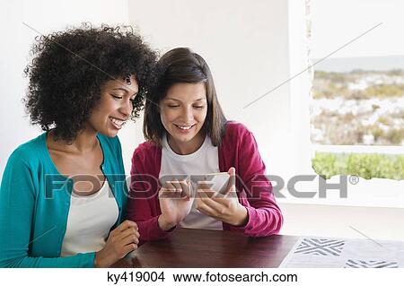 Friends using a mobile phone and smiling View Large Photo Image Picture - Friends using a mobile phone and smiling. Fotosearch