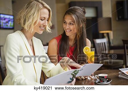 Stock Image - Two female friends looking at menu in a restaurant. Fotosearch