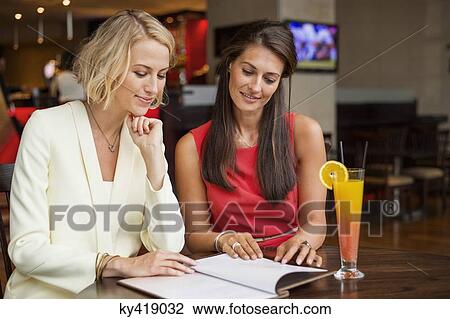 Stock Image - Two female friends looking at menu in a restaurant. Fotosearch