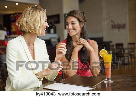 Two female friends smiling at each other in a restaurant View Large Photo Image Stock Image - Two female friends smiling at each other in a restaurant. Fotosearch