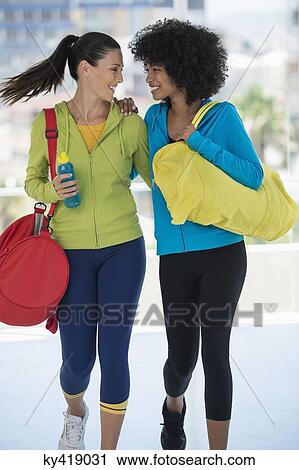 Stock Image - Two happy female friends carrying gym bags. Fotosearch