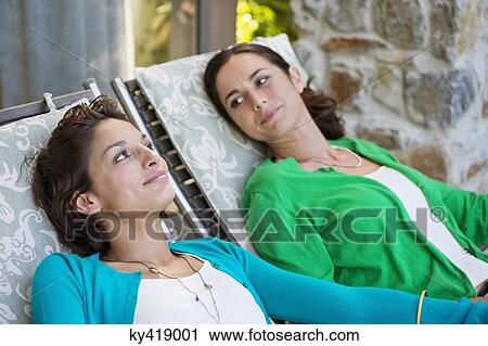 Stock Image - Two women relaxing on lounge chairs. Fotosearch