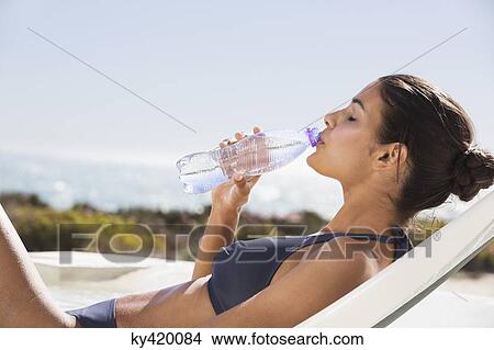 Picture - Beautiful woman drinking water on the beach. Fotosearch