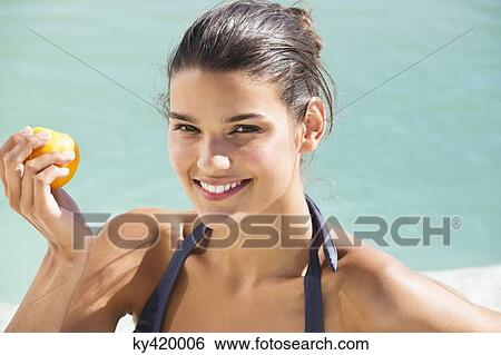 Stock Photograph - Beautiful woman eating a tomato on the beach. Fotosearch