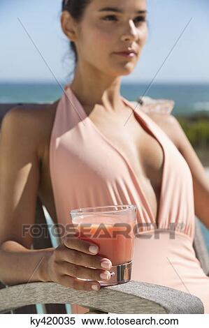 Beautiful woman holding a glass of juice and sitting on a chair on the beach View Large Photo Image Stock Photography - Beautiful woman holding a glass of juice and sitting on a chair on the beach. Fotosearch