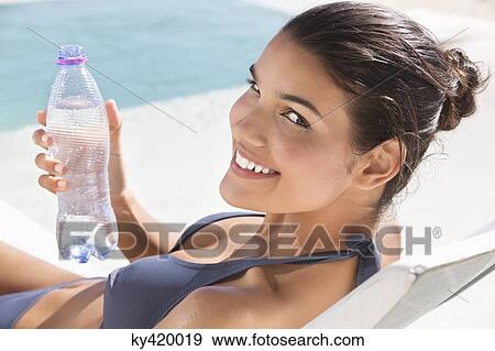 Beautiful woman holding a water bottle while sunbathing on the beach View Large Photo Image Stock Photo - Beautiful woman holding a water bottle while sunbathing on the beach. Fotosearch