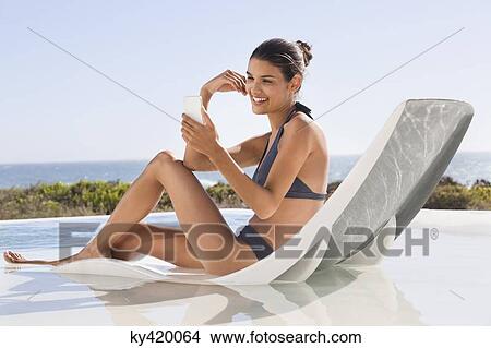 Beautiful woman video calling on cell phone while sunbathing on the beach View Large Photo Image Picture - Beautiful woman video calling on cell phone while sunbathing on the beach. Fotosearch