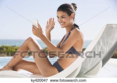 Beautiful woman video calling on cell phone while sunbathing on the beach View Large Photo Image Stock Photo - Beautiful woman video calling on cell phone while sunbathing on the beach. Fotosearch