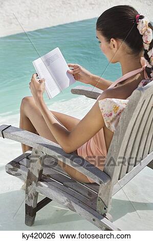 Woman sitting on a chair and reading a book on the beach View Large Photo Image Stock Photograph - Woman sitting on a chair and reading a book on the beach. Fotosearch
