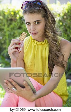 Portrait of a woman eating a chocolate and using a digital tablet View Large Photo Image Stock Photo - Portrait of a woman eating a chocolate and using a digital tablet. Fotosearch