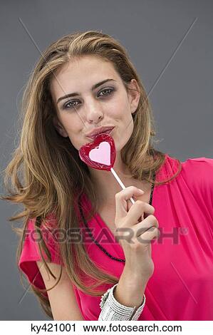 Stock Image - Portrait of a woman eating a heart shape lollipop. Fotosearch
