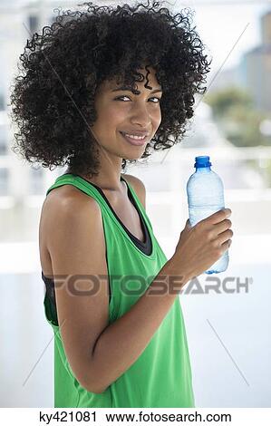 Stock Image - Portrait of a woman holding a water bottle and smiling. Fotosearch