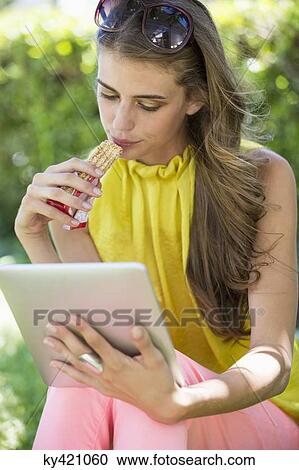 Woman eating chocolate and looking at a digital tablet View Large Photo Image Stock Image - Woman eating chocolate and looking at a digital tablet. Fotosearch