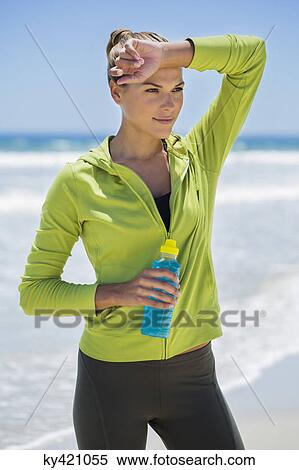Stock Photography - Woman holding a water bottle on the beach. Fotosearch
