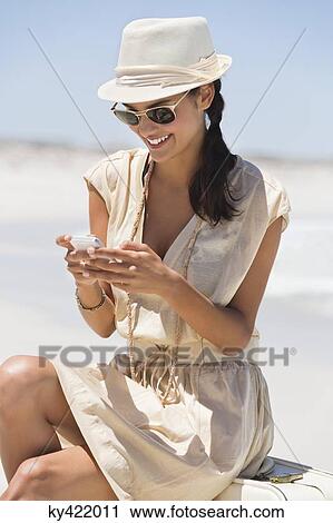 Stock Image - Beautiful woman text messaging on a cell phone on the beach. Fotosearch