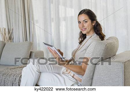 Beautiful woman using a digital tablet and smiling on a couch View Large Photo Image Stock Image - Beautiful woman using a digital tablet and smiling on a couch. Fotosearch