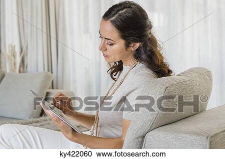 Beautiful woman using a digital tablet and smiling on a couch View Large Photo Image Stock Image - Beautiful woman using a digital tablet and smiling on a couch. Fotosearch