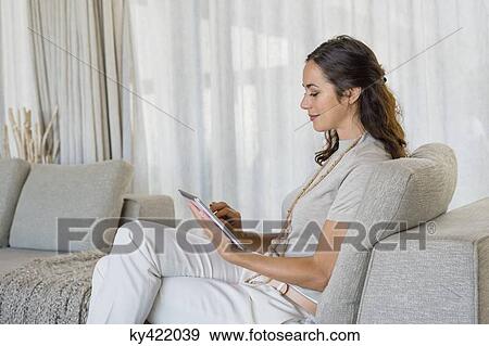 Beautiful woman using a digital tablet and smiling on a couch View Large Photo Image Stock Photo - Beautiful woman using a digital tablet and smiling on a couch. Fotosearch