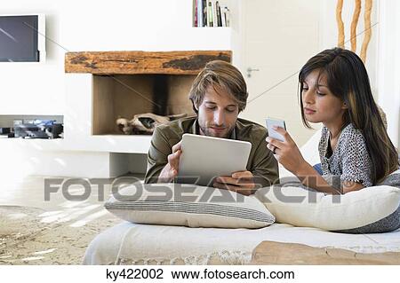 Stock Image - Couple lying on the bed and using electronic gadgets. Fotosearch