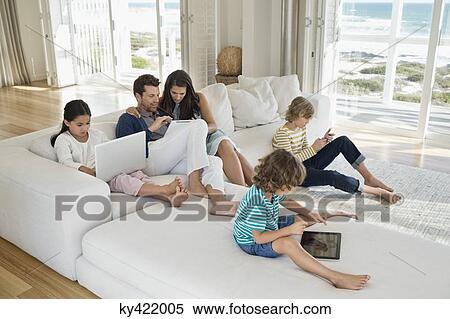Stock Photography - Family using electronic gadgets in a living room. Fotosearch