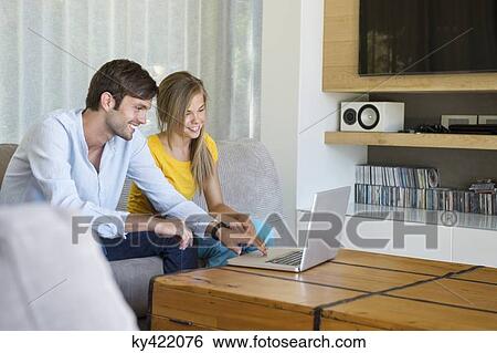 Man and his daughter sitting on a couch looking at a laptop View Large Photo Image Stock Photograph - Man and his daughter sitting on a couch looking at a laptop. Fotosearch