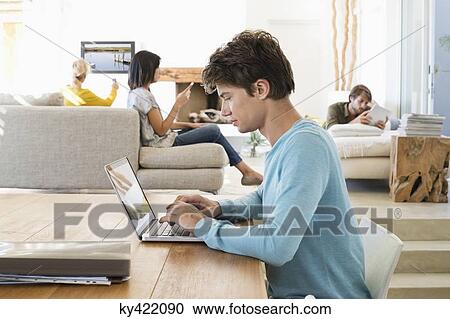 Man using a laptop with his friends using electronic gadgets in background View Large Photo Image Stock Image - Man using a laptop with his friends using electronic gadgets in background. Fotosearch