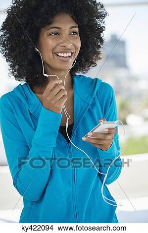 Smiling woman listening to music on a mobile phone View Large Photo Image Picture - Smiling woman listening to music on a mobile phone. Fotosearch