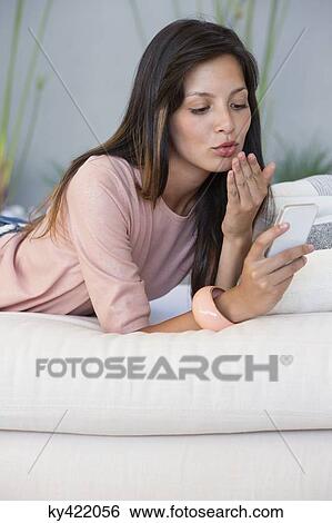 Woman reading text message on a mobile phone and giving flying kiss View Large Photo Image Stock Photograph - Woman reading text message on a mobile phone and giving flying kiss. Fotosearch