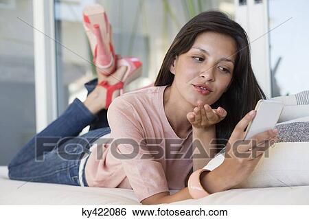 Woman reading text message on a mobile phone and giving flying kiss View Large Photo Image Stock Photograph - Woman reading text message on a mobile phone and giving flying kiss. Fotosearch