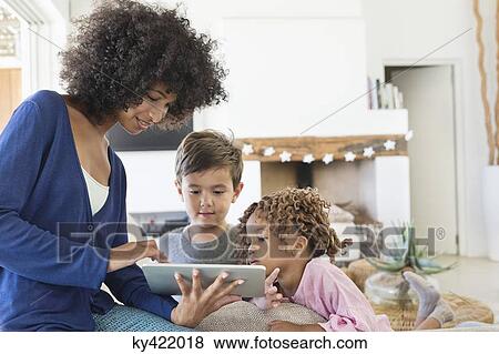 Stock Photo - Woman showing a digital tablet to her children. Fotosearch