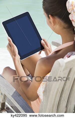 Stock Photography - Woman sitting on a chair and using digital tablet on the beach. Fotosearch