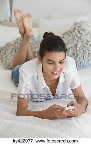 Woman text messaging on a cell phone on the bed View Large Photo Image Stock Photo - Woman text messaging on a cell phone on the bed. Fotosearch