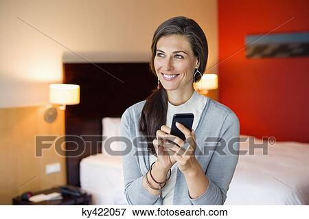 Stock Photo - Woman using a cell phone in a hotel room. Fotosearch