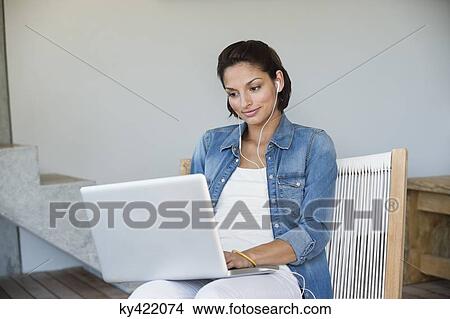 Woman using a laptop and listening to music View Large Photo Image Picture - Woman using a laptop and listening to music. Fotosearch