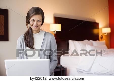 Stock Image - Woman using a laptop in a hotel room and smiling. Fotosearch