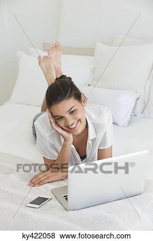 Woman using a laptop on the bed View Large Photo Image Stock Photo - Woman using a laptop on the bed. Fotosearch