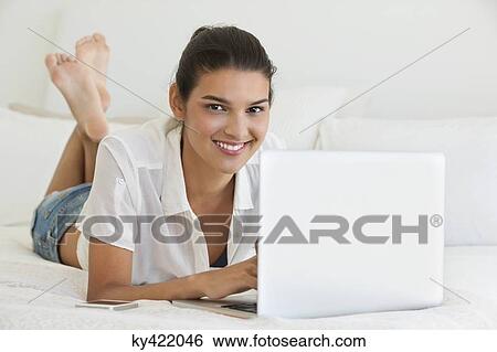 Woman using a laptop on the bed View Large Photo Image Stock Photograph - Woman using a laptop on the bed. Fotosearch