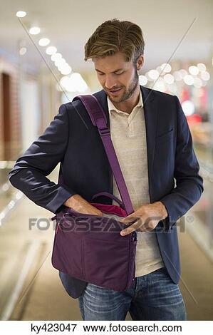 Man standing on an airport looking into a shoulder bag View Large Photo Image Stock Photo - Man standing on an airport looking into a shoulder bag. Fotosearch