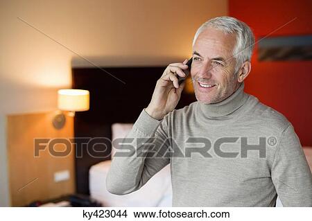 Picture - Man talking on a cell phone in a hotel room. Fotosearch