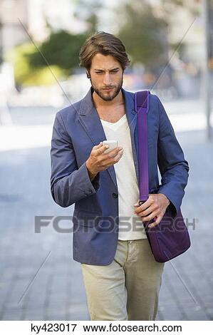 Man walking on a street using a mobile phone View Large Photo Image Stock Photo - Man walking on a street using a mobile phone. Fotosearch