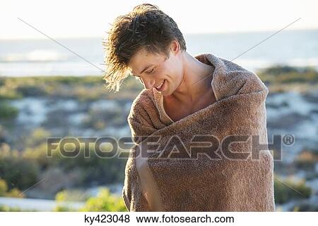 Stock Photo - Man wrapped in a towel standing on the beach. Fotosearch