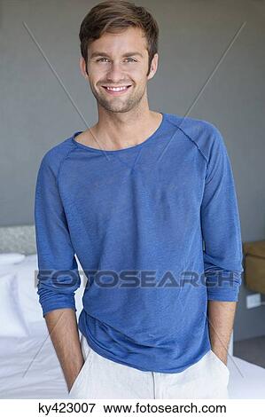 Stock Photo - Portrait of a man smiling with his hands in pockets in bedroom. Fotosearch