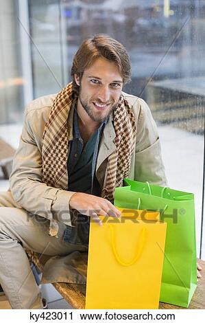 Stock Image - Portrait of a smiling man sitting at an airport lounge with shopping bags. Fotosearch