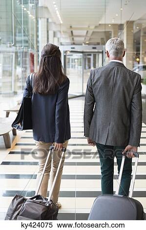 Stock Photography - Business couple pulling suitcases in a hotel lobby. Fotosearch