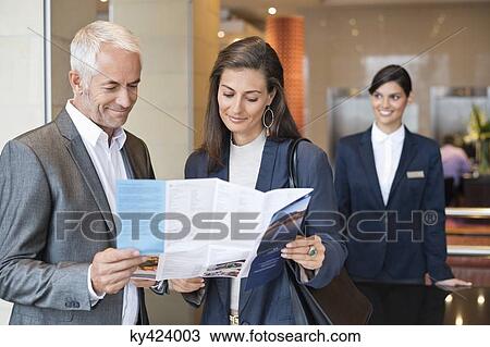 Business couple reading a brochure in front of a hotel reception counter View Large Photo Image Stock Image - Business couple reading a brochure in front of a hotel reception counter. Fotosearch