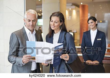 Business couple reading a brochure in front of a hotel reception counter View Large Photo Image Stock Image - Business couple reading a brochure in front of a hotel reception counter. Fotosearch