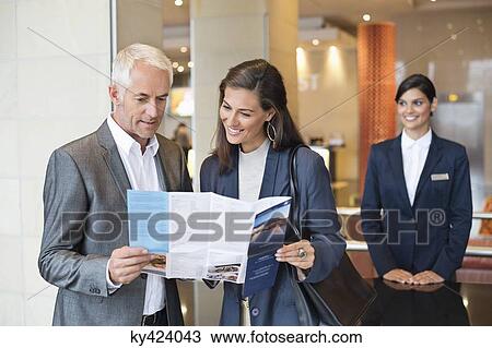 Business couple reading a brochure in front of a hotel reception counter View Large Photo Image Stock Image - Business couple reading a brochure in front of a hotel reception counter. Fotosearch